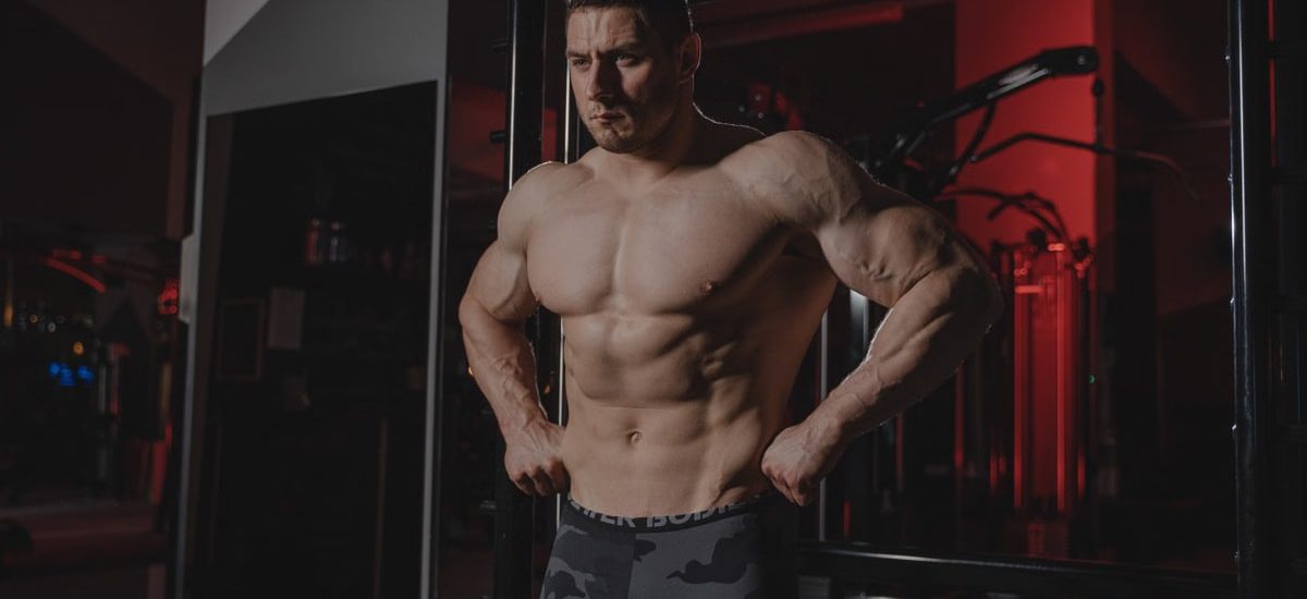 Shirtless bodybuilder flexing muscles under dramatic gym lighting. Fitness and strength.